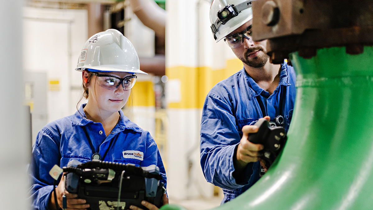 Bruce Power Environment and Sustainability Fund Woman and man, wearing a hardhat and safety goggles, inspecting equipment.
